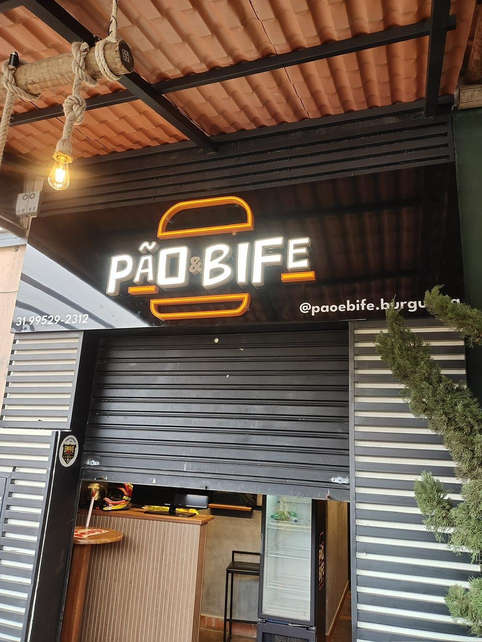 Fachada frontal da Pão & Bife com painel preto brilhante, telefone e perfil de Instagram.