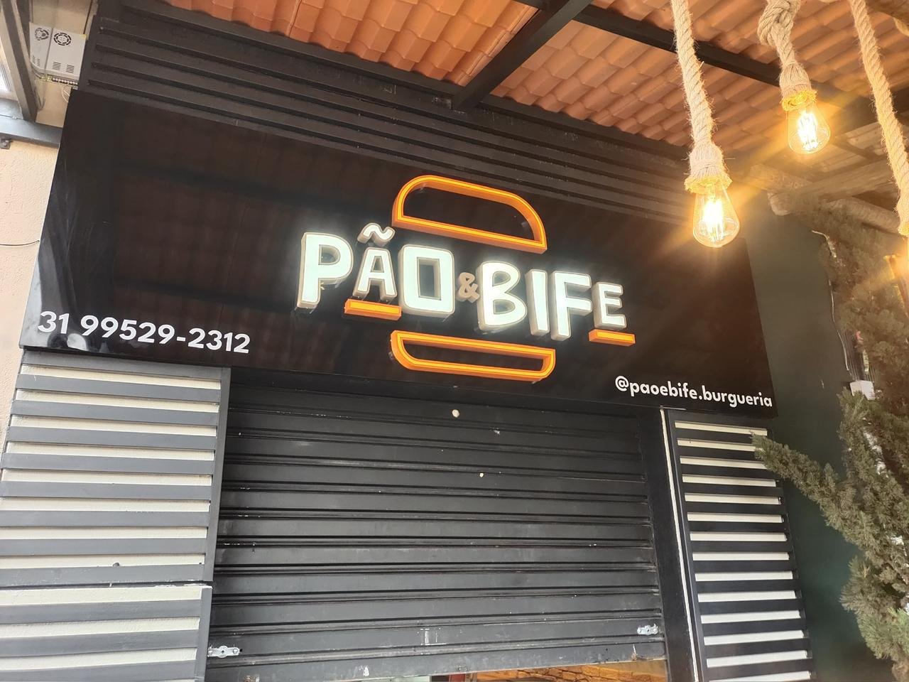 Fachada da Pão & Bife com letreiro neon branco e laranja vista com parte do interior aparente.