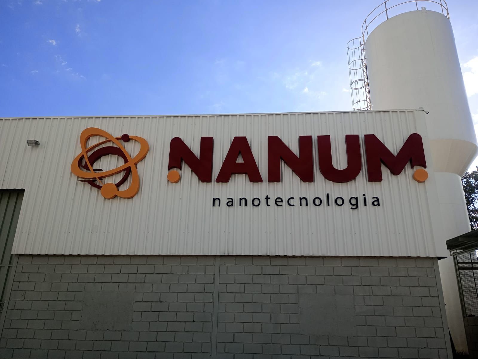 Letreiro externo da Nanum Nanotecnologia com símbolo laranja e letras volumétricas vinho.