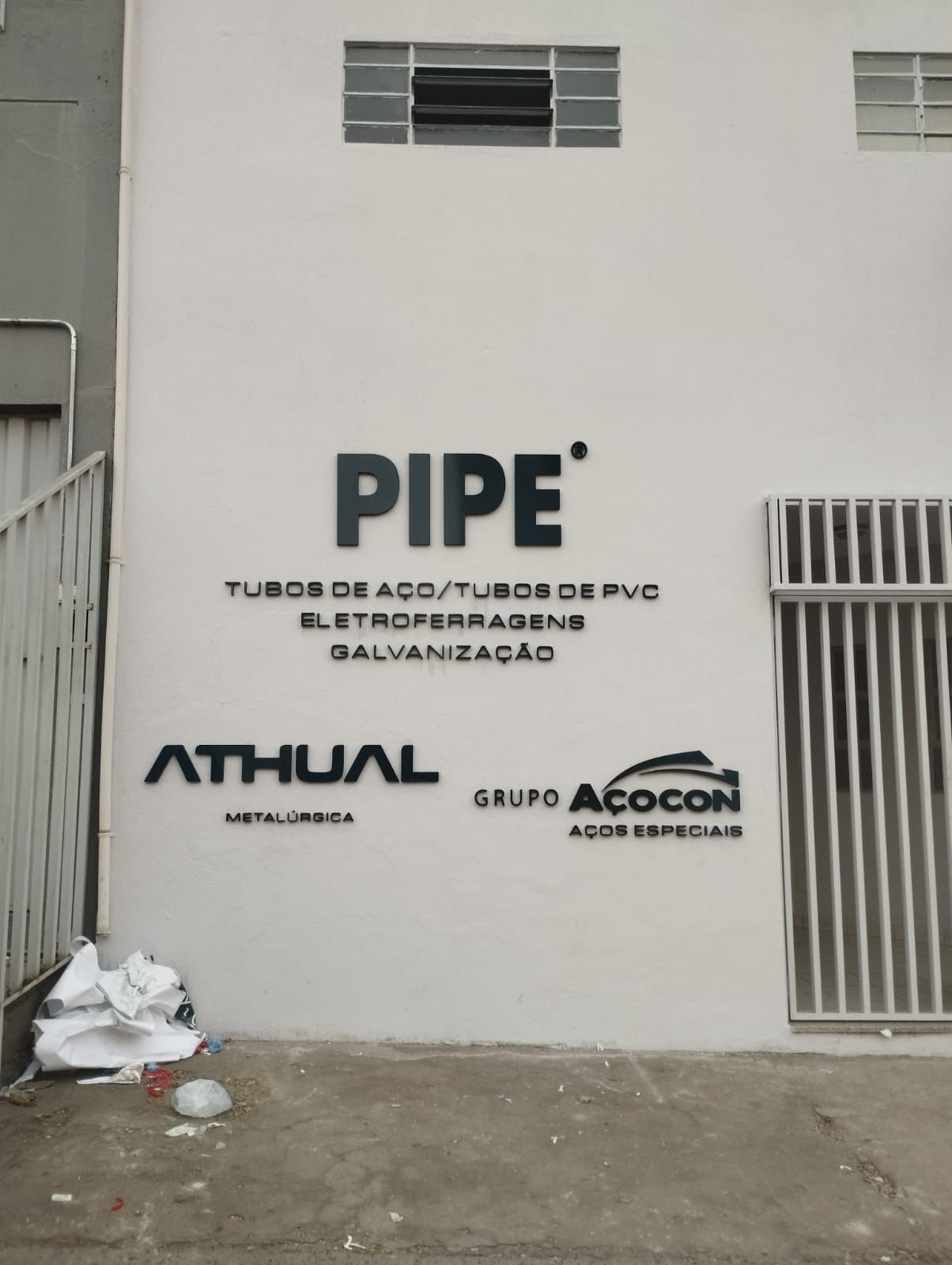 Letreiros aplicados em parede externa clara com marcas corporativas em relevo.