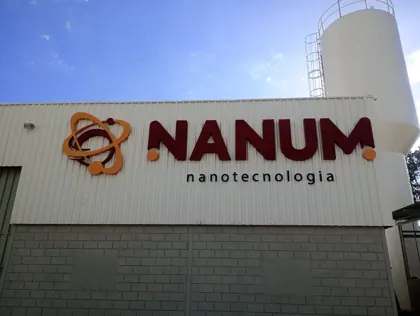 Miniatura: Letreiro externo da Nanum Nanotecnologia com símbolo atômico em laranja e tipografia volumétrica vinho.