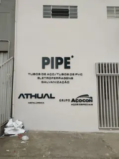 Miniatura: Parede externa com letreiros da PIPE, Athual Metalúrgica e Grupo Acocon em acabamento escuro.
